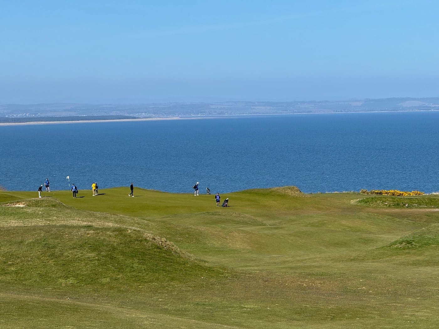 Golfers on a coastal links green above the ocean