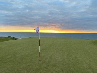 A flag against the ocean sunset on a links green
