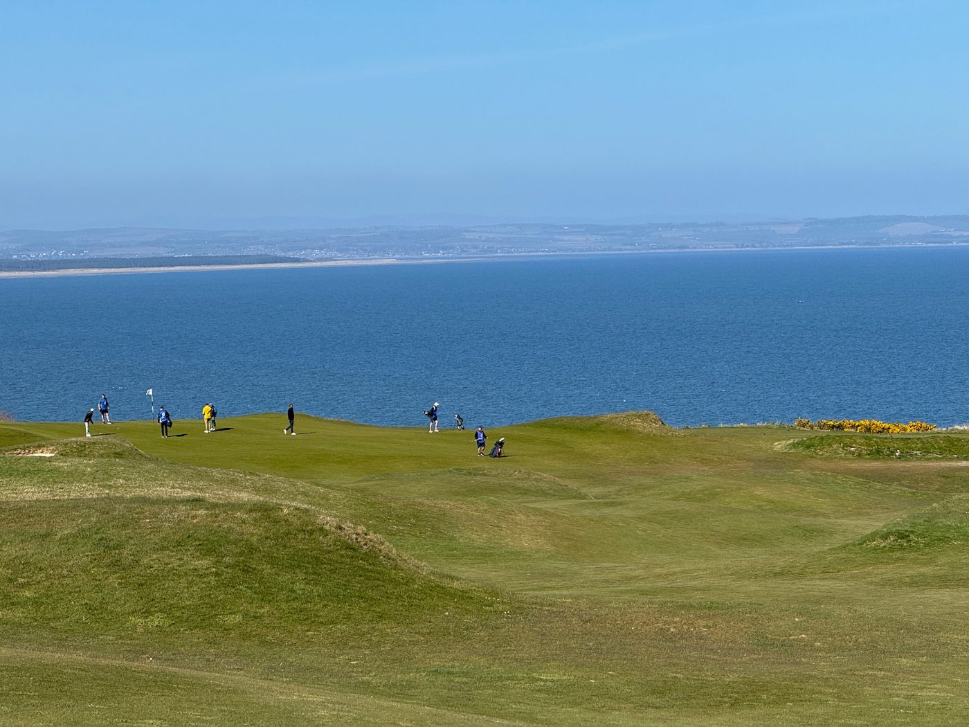 Golfers on a coastal links green above the ocean